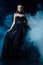 Vampire girl in black gothic dress on black background with smoke