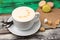 Vanilla cappuccino in a white cup with sugar and macaroons on wooden table