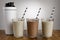 Vanilla, coconut and Chocolate milkshakes, with paper straws and shaker on a wooden bench top