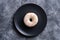 Vanilla donut with sprinkles on black plate, sweet glazed dessert food on concrete textured background