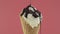 Vanilla ice cream with chocolate sauce in waffle cone over pink background