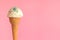 vanilla ice cream in waffle cone with strewed multicolor sprinkles on pink background