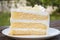 Vanilla sponge cake with cream and white chocolate decorate. Sliced piece of cake on white plate. Served on wooden table.