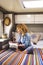 Vanlife and relax. Serene woman reading a book sitting on bed inside camper van bedroom. Relaxation and travel nomadic lifestyle