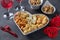 Varieties of elite cheese in a heart-shaped plate, cashews, peanuts and two glasses of wine for Valentine's Day on dark
