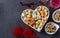 Varieties of elite cheese in a heart-shaped plate, cashews, peanuts and two glasses of wine for Valentine's Day on gray