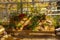 A variety of autumn flowers in ceramic pots and vegetables in baskets stand on a shelf covered with burlap and straw.