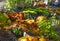 A variety of autumn flowers in ceramic pots and vegetables in baskets stand on a shelf covered with burlap and straw.