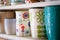 A variety of ceramic mugs and cups in spring floral bright style stand in a row on a white home shelf.