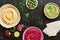 A variety of colored hummus, pita bread, olives, pomegranate on a dark woody background. Top view, place for text.