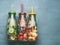 Variety of colorful infused water in bottles with fruits berries, cucumber, herbs and drink straws on gray background, top view.