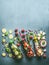 Variety of colorful infused water in bottles with fruits berries, cucumber, herbs and drink straws with ingredients on table, top