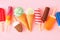 Variety of colorful summer popsicles and ice cream treats on a pink background