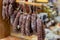 Variety of delicious dried sausages hanged on wooden rack at local farmer market. Fresh tasty meat delicatessen at butcher store