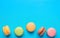 Variety of Multicolored Pink Green Yellow Brown Mocha Coffee Macaroons Scattered on Blue Background Bottom Border