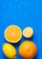 Variety of ripe organic citrus fruits halved whole oranges sliced lemons on blue background with water drops. Summer refreshment