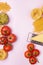 Variety of Types and Shapes of Dry Pasta Spaghetti Tagliatelle Fusilli Raw Tomatoes Bowl of Pesto Parmesan Cheese Top View Pink