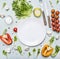 Variety of vegetables laid out around a white plate with oilknife and fork wooden rustic background top view close up