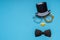 Various black photo booth props: cylinder hat, glasses, bow tie and nose in heart shape on blue background. Greeting card for