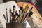 Various brushes in a ceramic container, in the background an open book