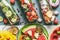 Various colorful infused water in bottles with fruits berries, cucumber, herbs with ingredients on table background, top view.