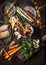 Various colorful organic vegetables ingredients from local market on dark rustic kitchen table background with pot, spoon, plates