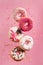 Various decorated doughnuts in motion falling on pink background