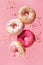 Various decorated doughnuts in motion falling on pink background