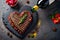 Various degrees of doneness of heart-shaped beef steak with spices, flowers and a bottle of wine on a stone dark