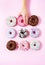 Various donuts on a pink background. A woman`s hand taking one.