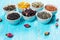 Various dried medicinal herbs and teas in several bowls on blue wooden background