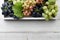 Various grapes with leaves in white wooden tray