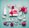 Various greeting LOVE objects: bottle of champagne, gift box, ribbon, flowers, bow, glasses and hearts on light blue desktop, top