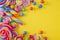 Various lollipops and round candy in bright and bold colours on a yellow background, with space for text