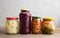 Various pickled, fermented, pickled vegetables in glass jars of different sizes stand on a wooden brown table. Cauliflower, red