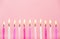 Various pink color birthday cake candles burning in line on pastel pink background.