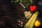 Various sorts of pasta on top of a dark wooden background. Farfalle, fusilli, spaghetti, bell pepper, corn salad