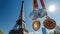 Various sports medals, gold, silver, bronze against background of Eiffel Tower under blue sky. Summer Olympics in Paris