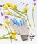 Various spring flowers and garden work gloves on white wooden background, top view.