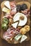 Various types of cheeses, grapes, walnuts and honey and prosciutto. Wooden cutting board