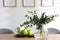 Vase with beautiful bouquet, apples and cup of drink on table indoors. Stylish interior design