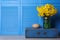 Vase with beautiful daffodils on wooden crate near light blue folding screen indoors, space for text