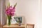 Vase with beautiful pink gladiolus flowers, pictures and cup on wooden table in room