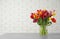 Vase with beautiful spring tulip flowers on table near brick wall.