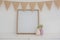 Vase, bunting and blank picture frame against white wall