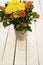 Vase of flowers on a white rustic table. Top view. Rustic vase with orange roses and yellow chrysanthemums. White background, empt