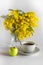 Vase of glass with branches of a mimosa, cup po coffee and apple on a white background