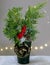 A vase with thuja branches and a pine cone is decorated with a golden rosette and fairy lights