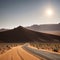 A vast African landscape scene, with a dirt road running through barren flat plains in the Namib Desert toward the
