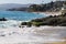 Vast blue ocean water crashing into the rocks along the beach with homes along the coastline with lush green palm trees